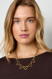 vrouw met goudkleurige hartjesketting bij donkerbruine top