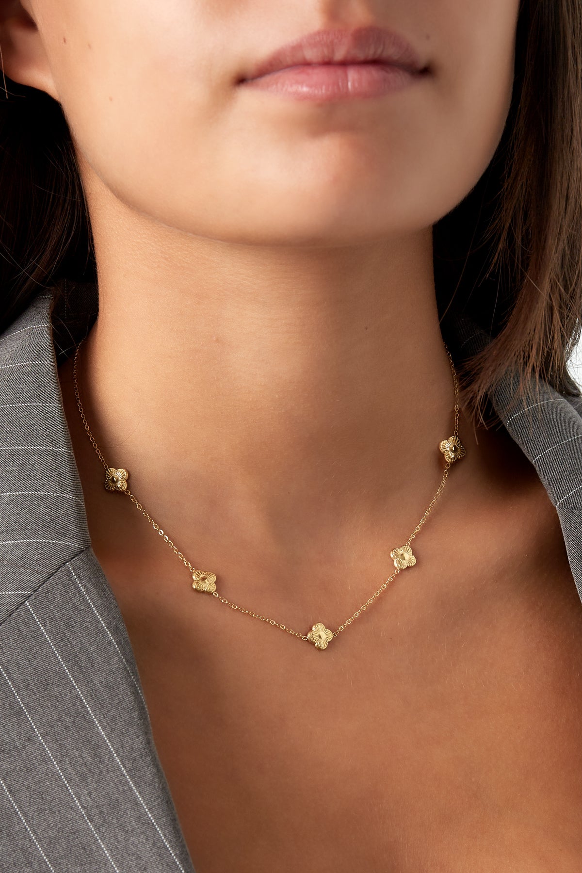 Model draagt gouden ketting met klaverpatroon bij grijs jasje