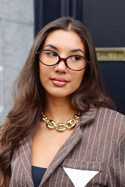 Vrouw met Ketting Luxe Schakels goud, kijkend naar voren met blazer en bril