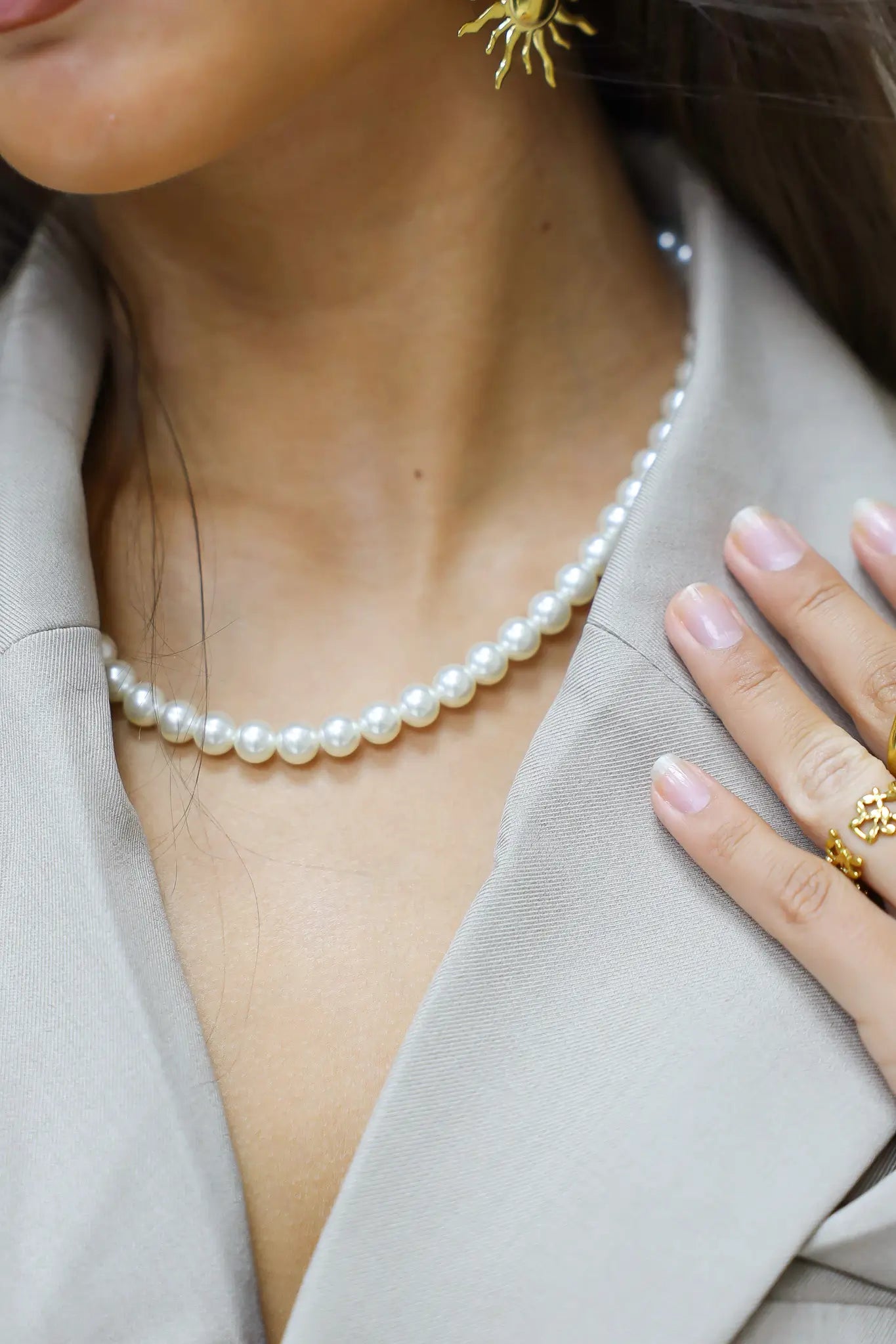 close up witte parelketting rond de hals met lichtgrijze blazer