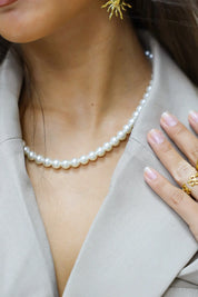 close up witte parelketting rond de hals met lichtgrijze blazer