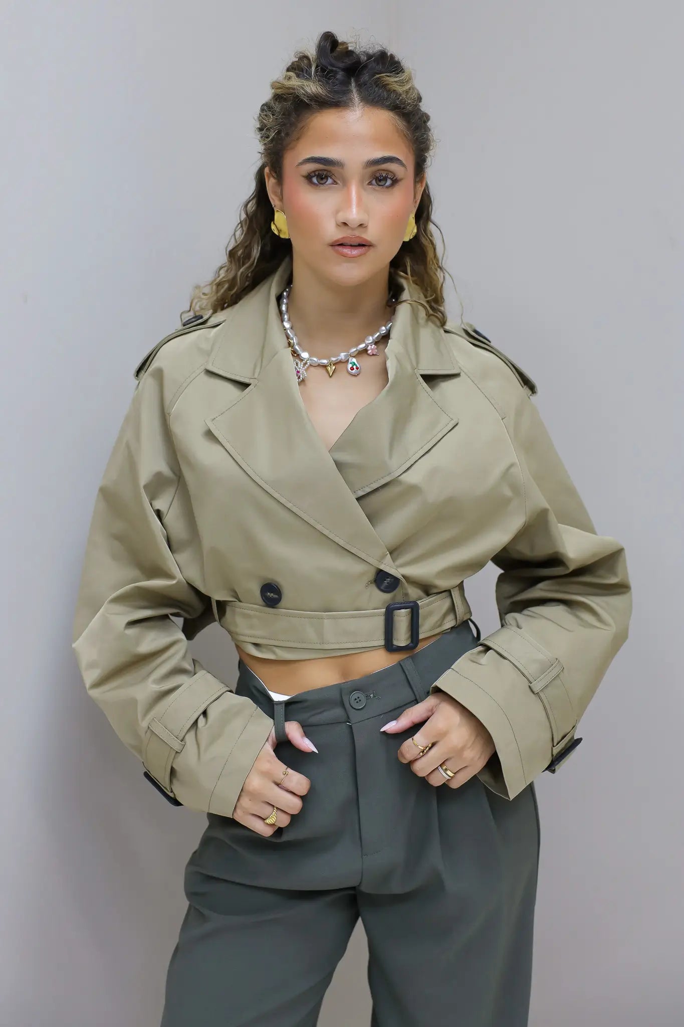 model met beige trenchcoat en gouden halsketting met parels en charms