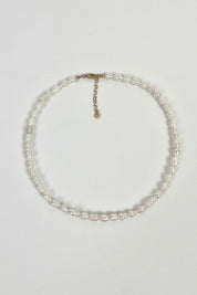 gouden halsketting met witte parels op lichte achtergrond