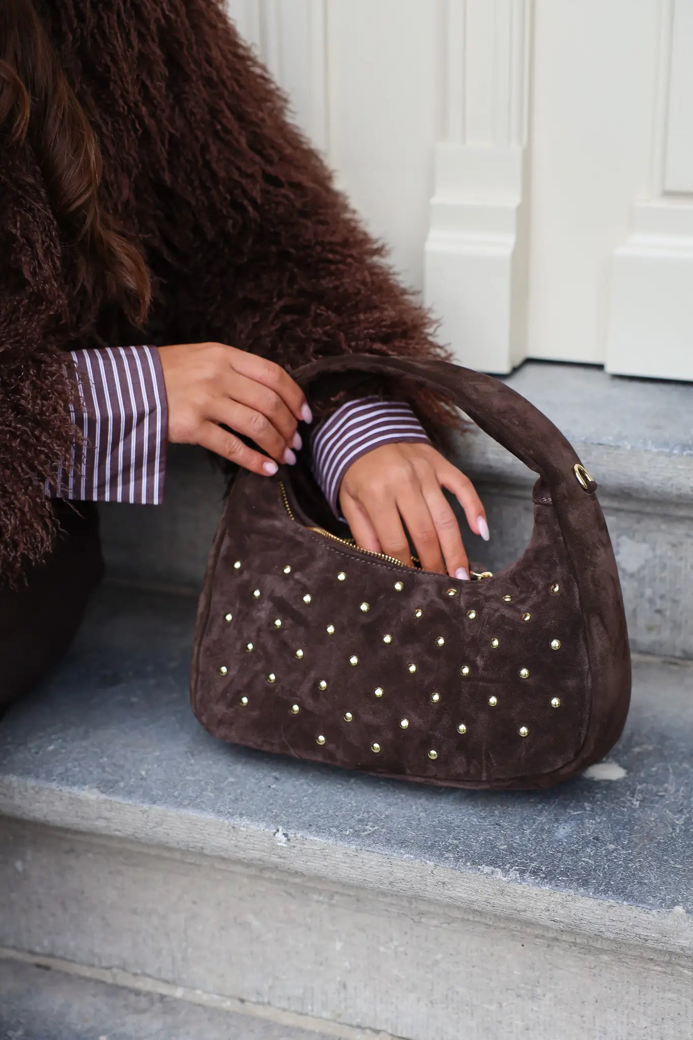 Close-up van de bruine suède tas met studs in hand van model