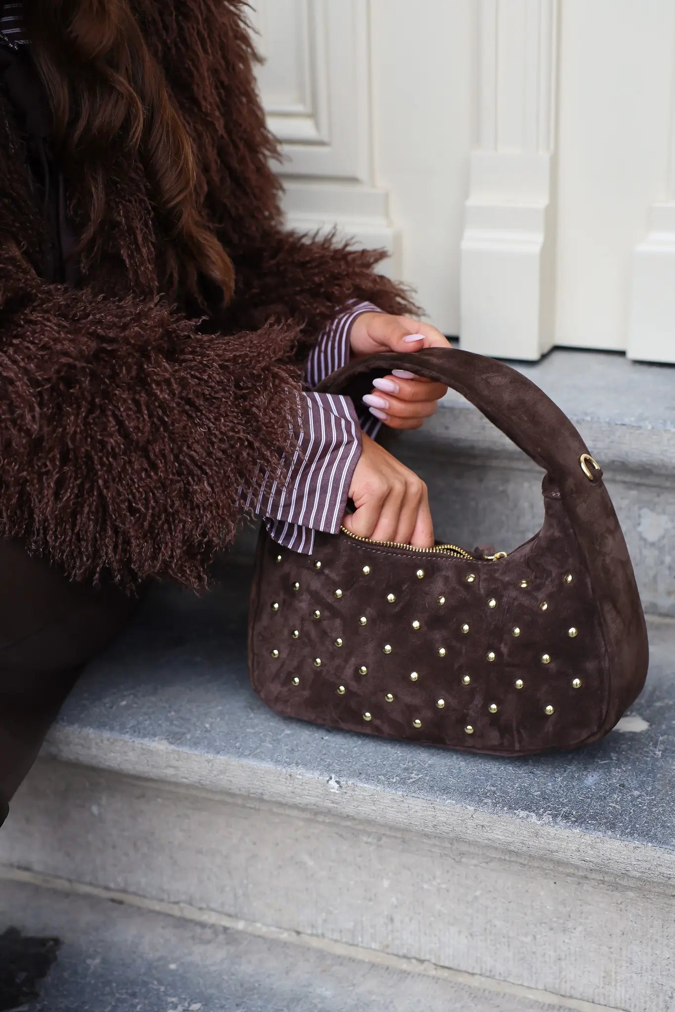 Model houdt de bruine suède tas met studs vast zittend op trap