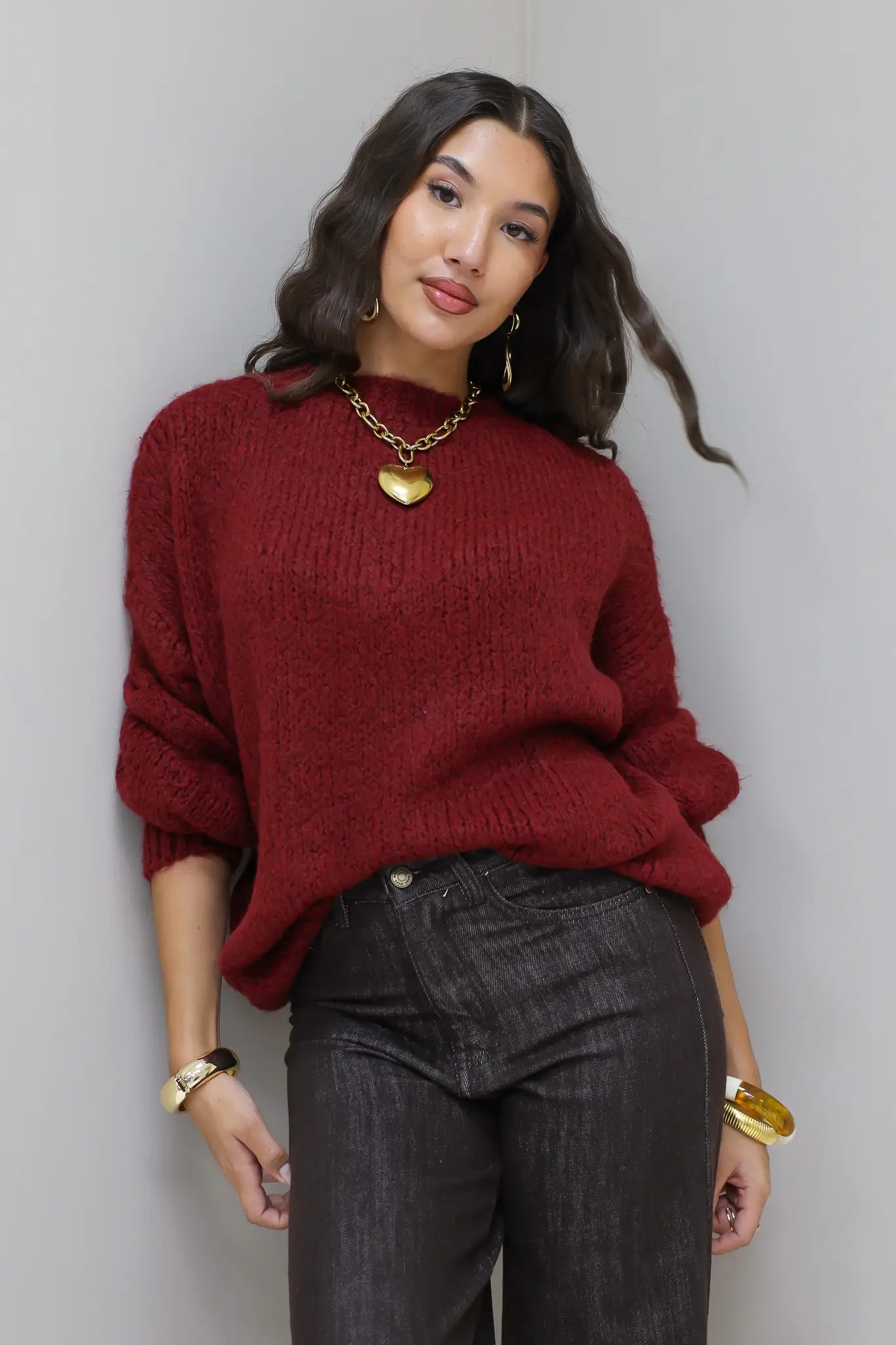 Model draagt de Liva trui bordeaux, licht cropped met gouden sieraden