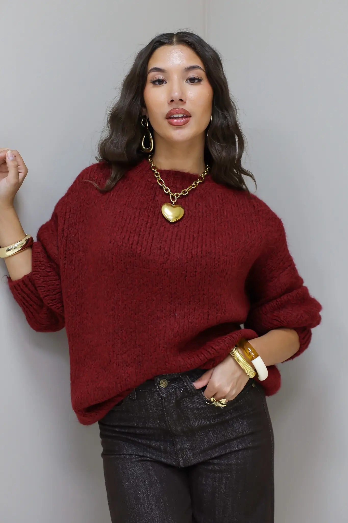 Model draagt de Liva trui bordeaux met donkere broek en gouden accessoires