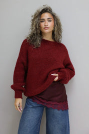 model draagt bordeaux trui over een rode top met kant en spijkerbroek