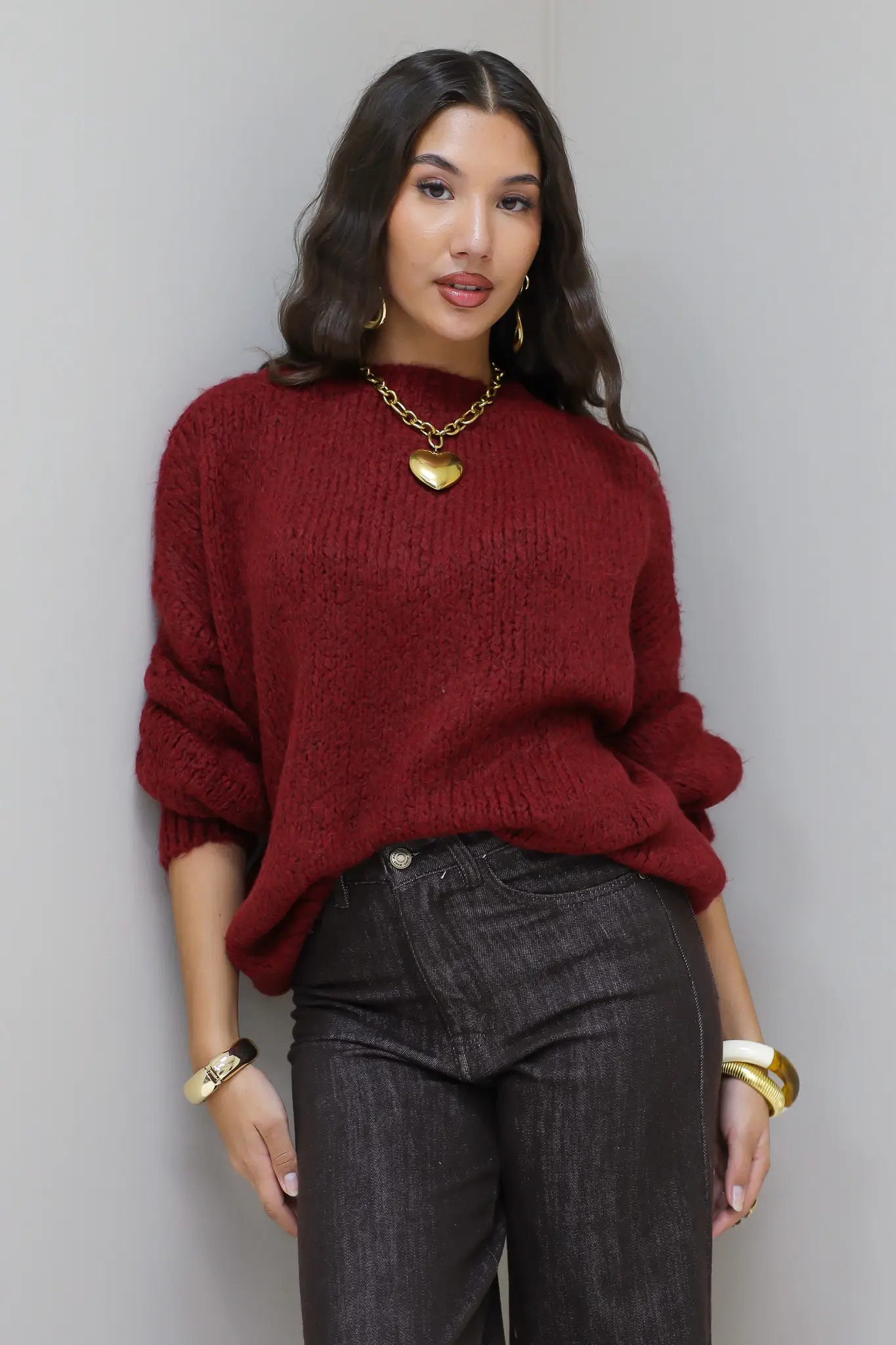 Model poseert voor lichte muur in de Liva trui bordeaux met bruine broek