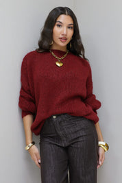 Model poseert voor lichte muur in de Liva trui bordeaux met bruine broek