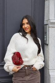 Model draagt de Liva trui wit met bruine broek en rode tas bij zwarte deur