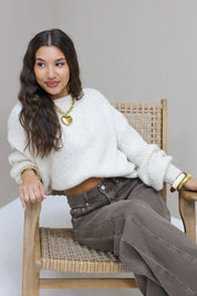 Model zit op stoel in de Liva trui wit met bruine broek en sieraden