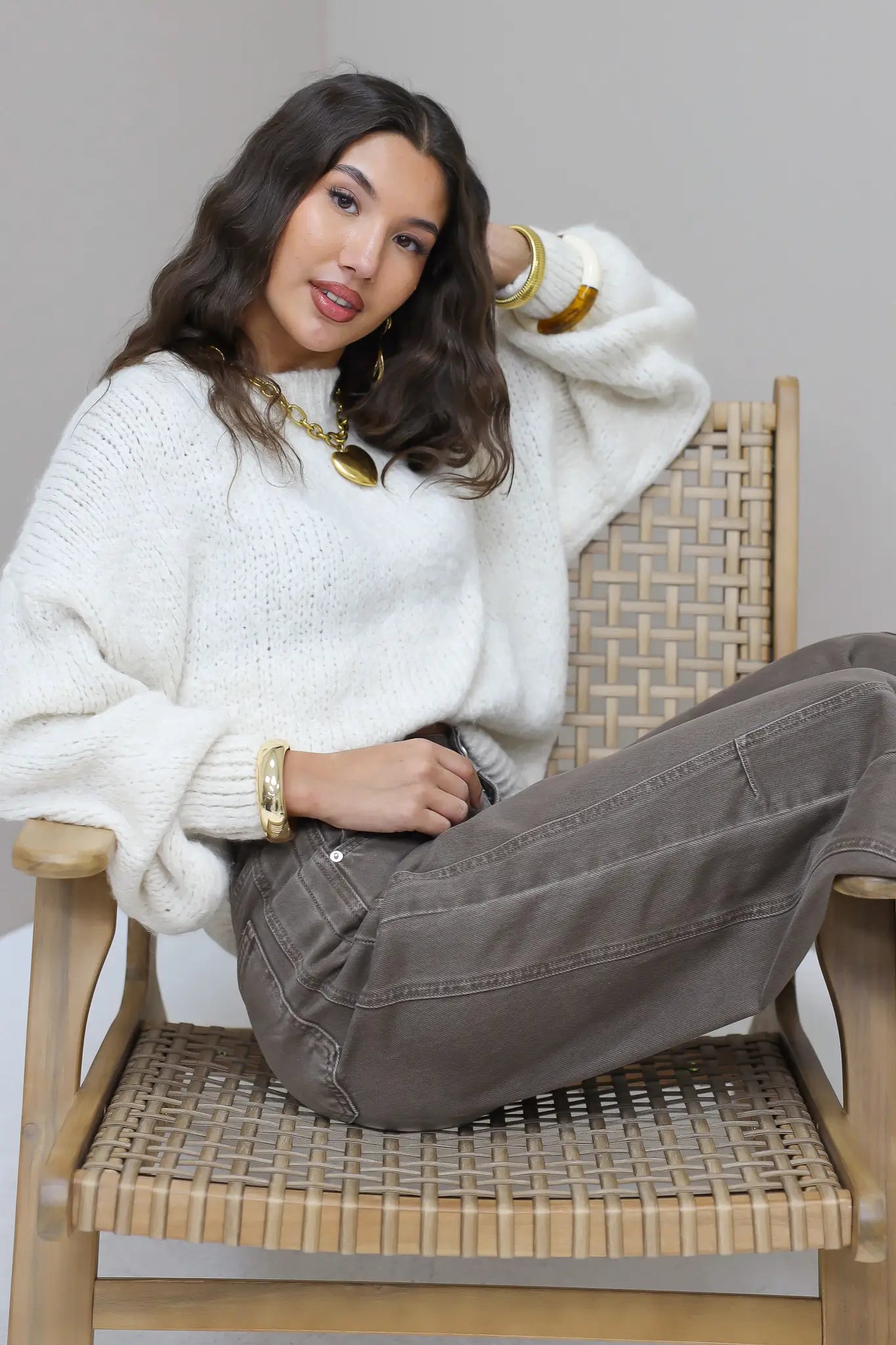 Model leunt op stoel in de Liva trui wit met bruine broek
