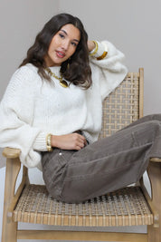 Model leunt op stoel in de Liva trui wit met bruine broek