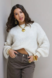 Model zit recht op stoel in de Liva trui wit met bruine broek