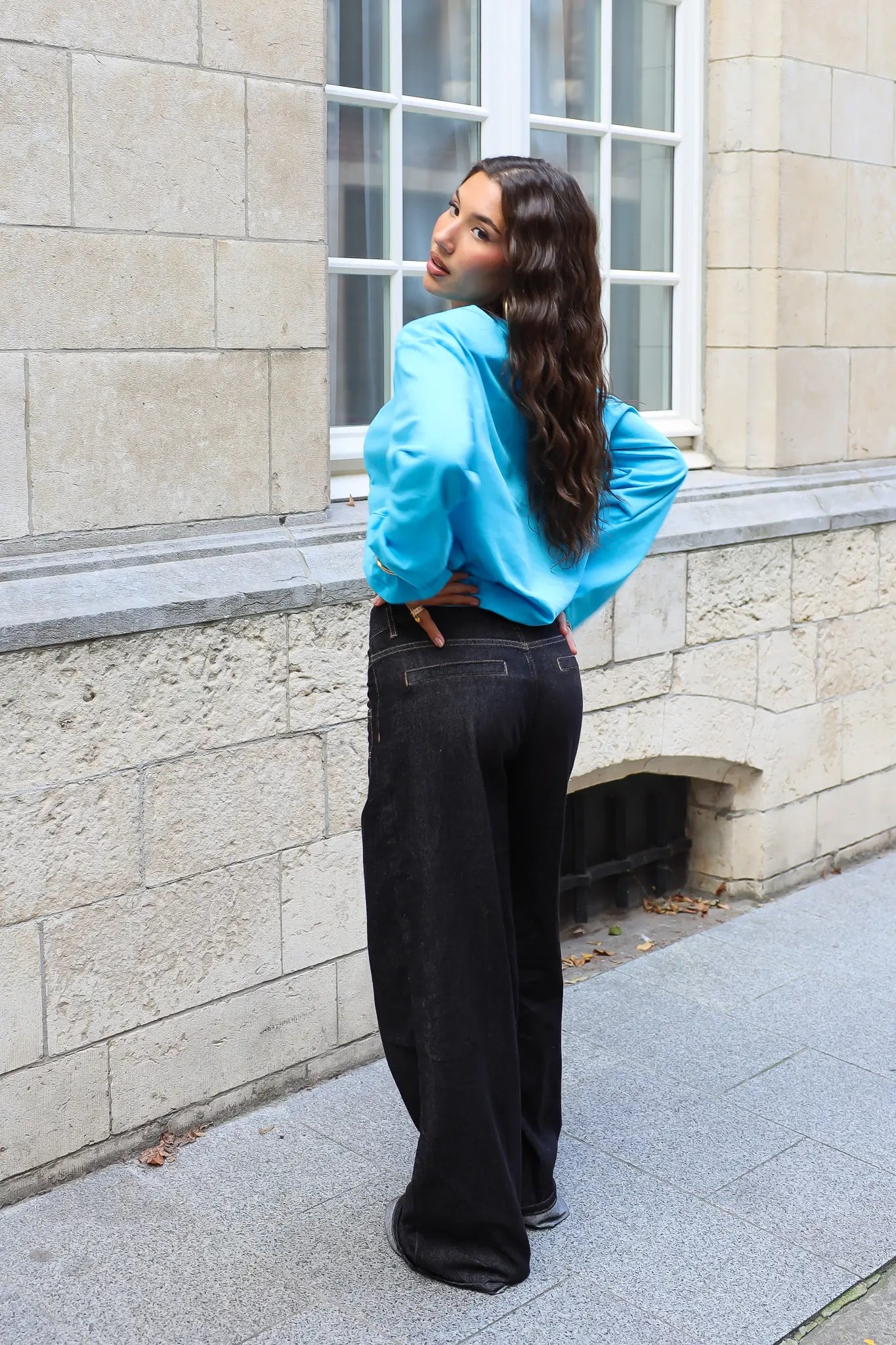 Achteraanzicht van de blauwe dames longsleeve met lange mouwen, gecombineerd met een zwarte wide leg jeans