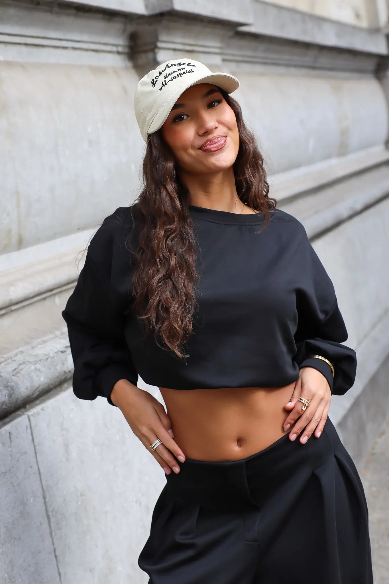 Beige Los Angeles baseball pet gecombineerd met zwarte cropped sweater en zwarte broek