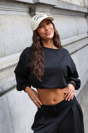 Beige Los Angeles baseball pet gecombineerd met zwarte cropped sweater en zwarte broek