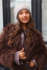 Vrouw met taupe muts zittend bij witte deur met tas