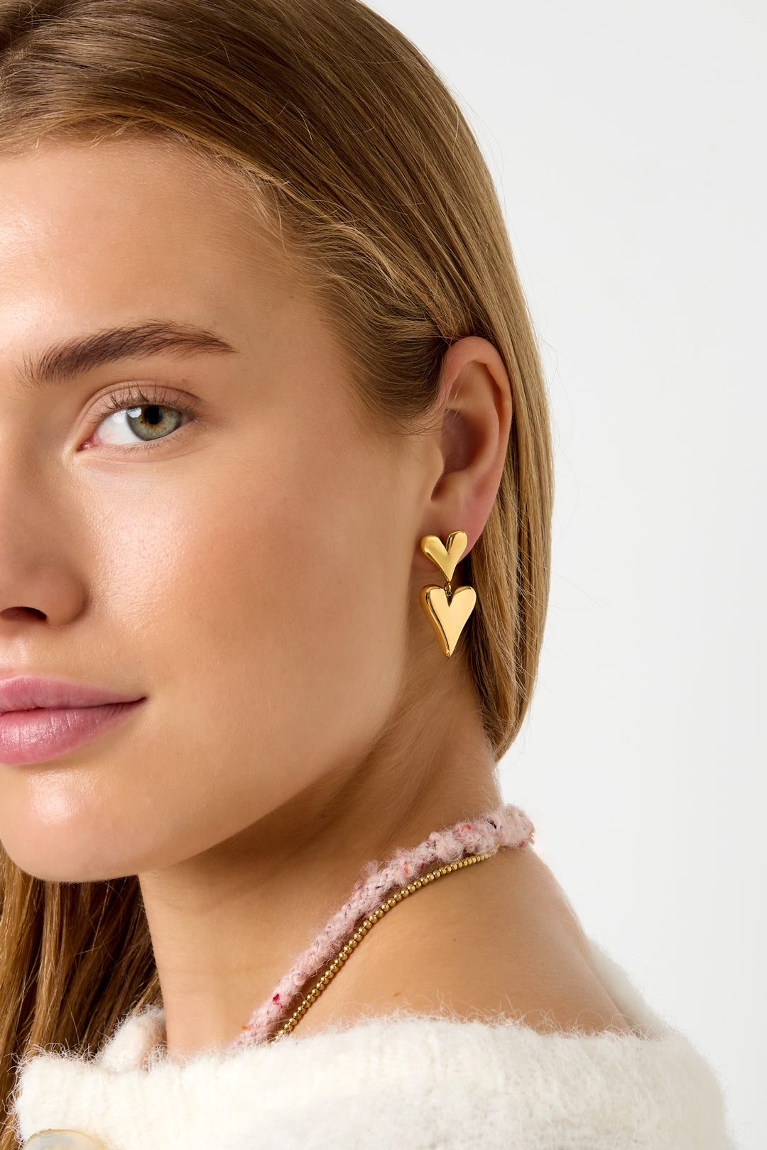 Model draagt gouden oorbellen met twee hartjes in close-up