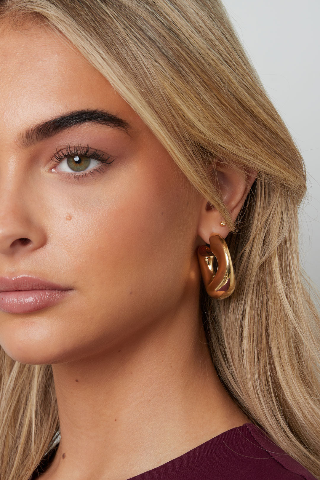 Vrouw met halflang blond haar draagt ronde gouden oorbellen