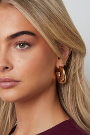 Vrouw met halflang blond haar draagt ronde gouden oorbellen