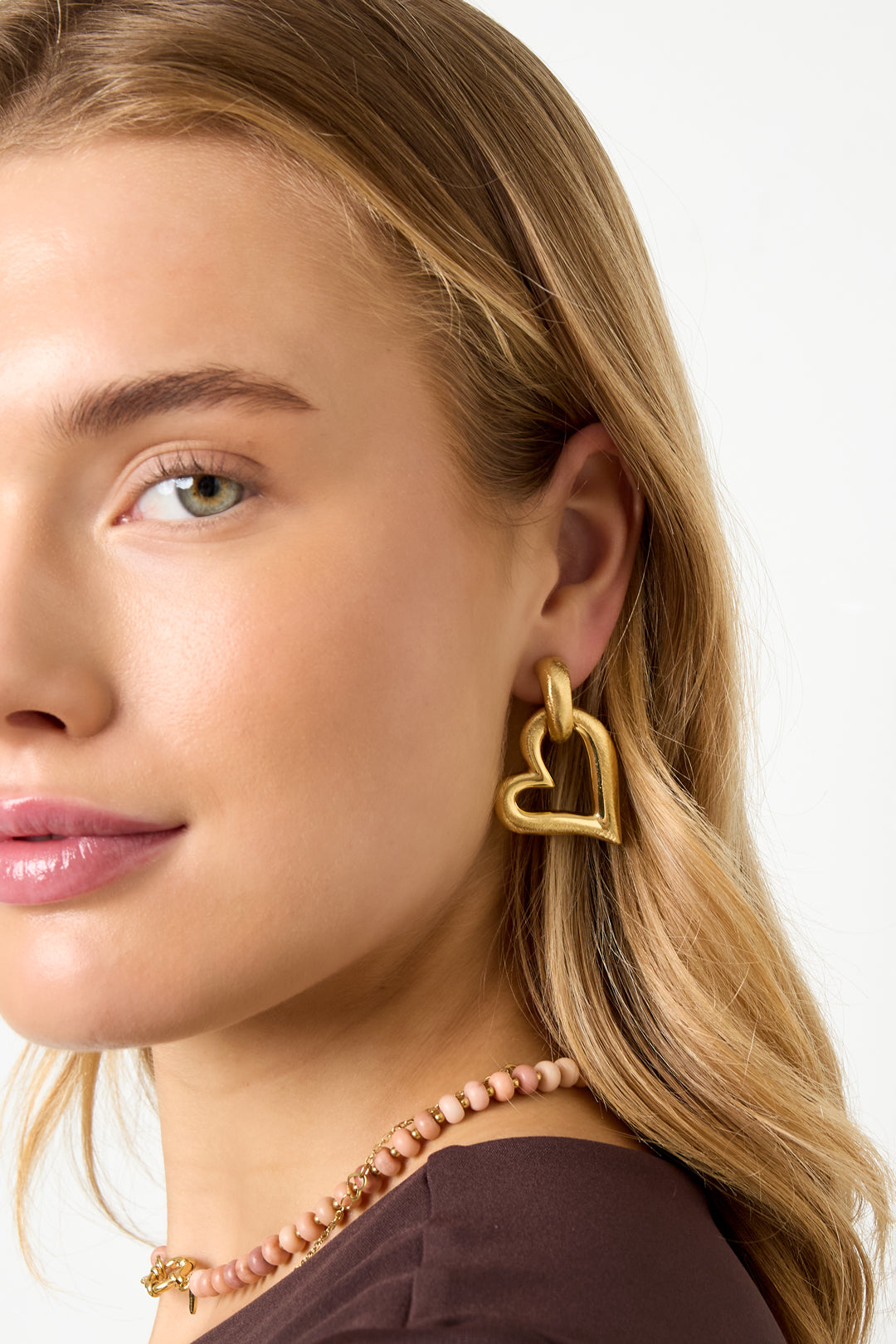 Model met blonde haren draagt grote gouden hart oorbellen