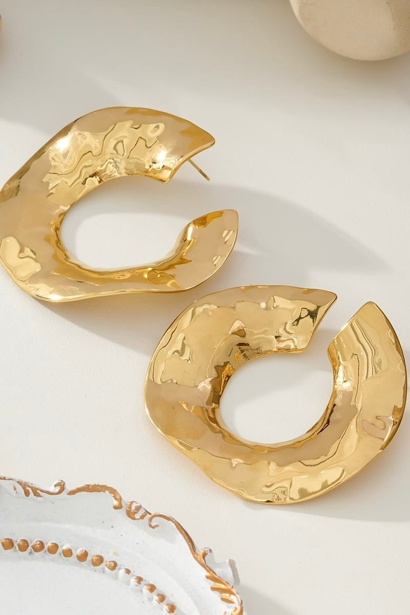 Organische goudkleurige oorringen op lichte achtergrond