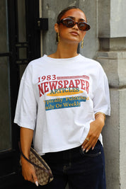 Oversized wit newspaper shirt met korte mouwen en opvallende rode gele en blauwe opdruk gedragen met een zonnebril