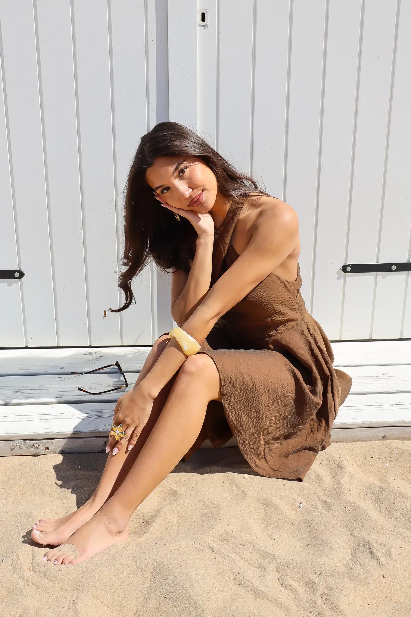 Model zit in zand met overslag jurk bruin