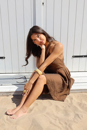 Model zit in zand met overslag jurk bruin