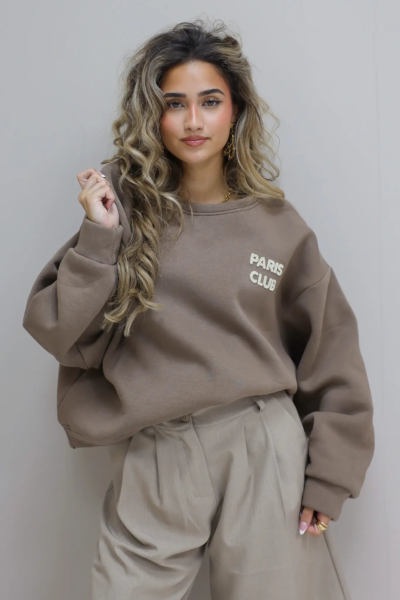 Paris Club Sweater in beige staand tegen grijze muur
