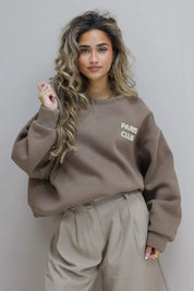 Paris Club Sweater in beige staand tegen grijze muur