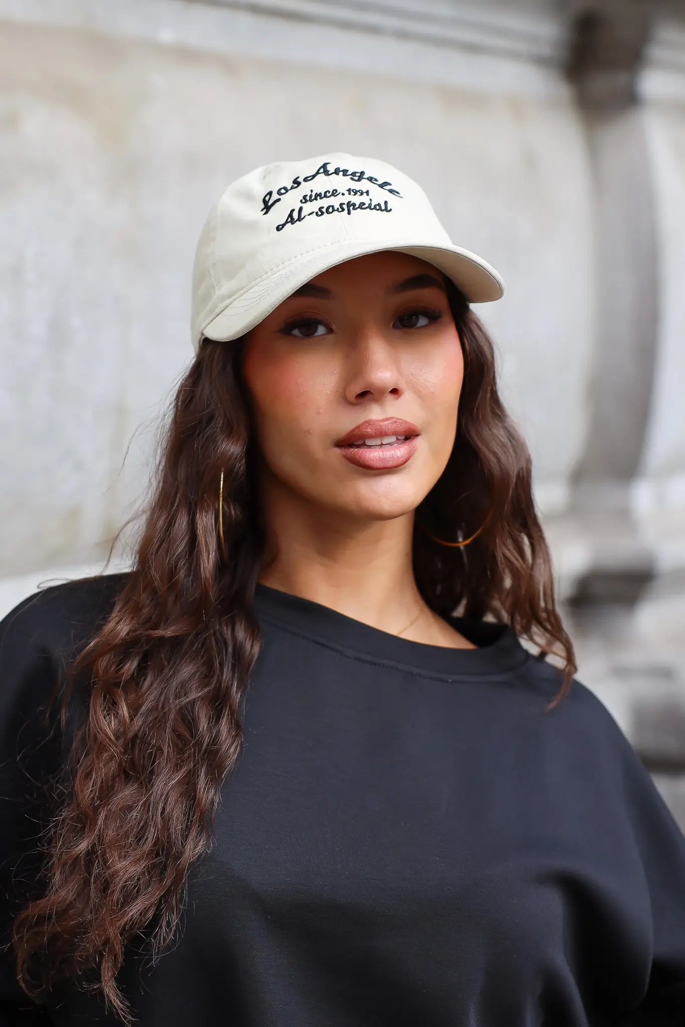 Beige Los Angeles pet met zwarte geborduurde tekst en gebogen klep gedragen met zwarte sweater