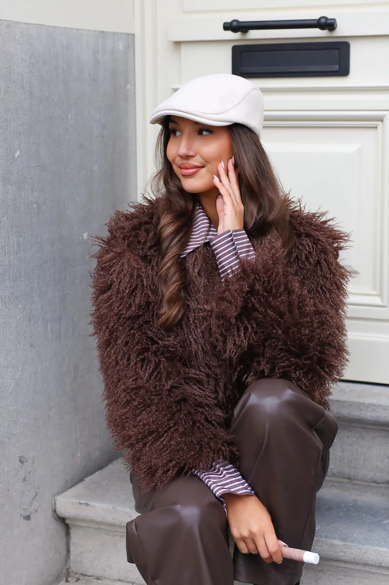 Vrouw met beige pet leunend tegen muur buiten