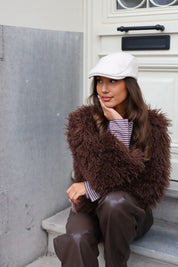 Vrouw met beige pet zittend bij deur met handtas