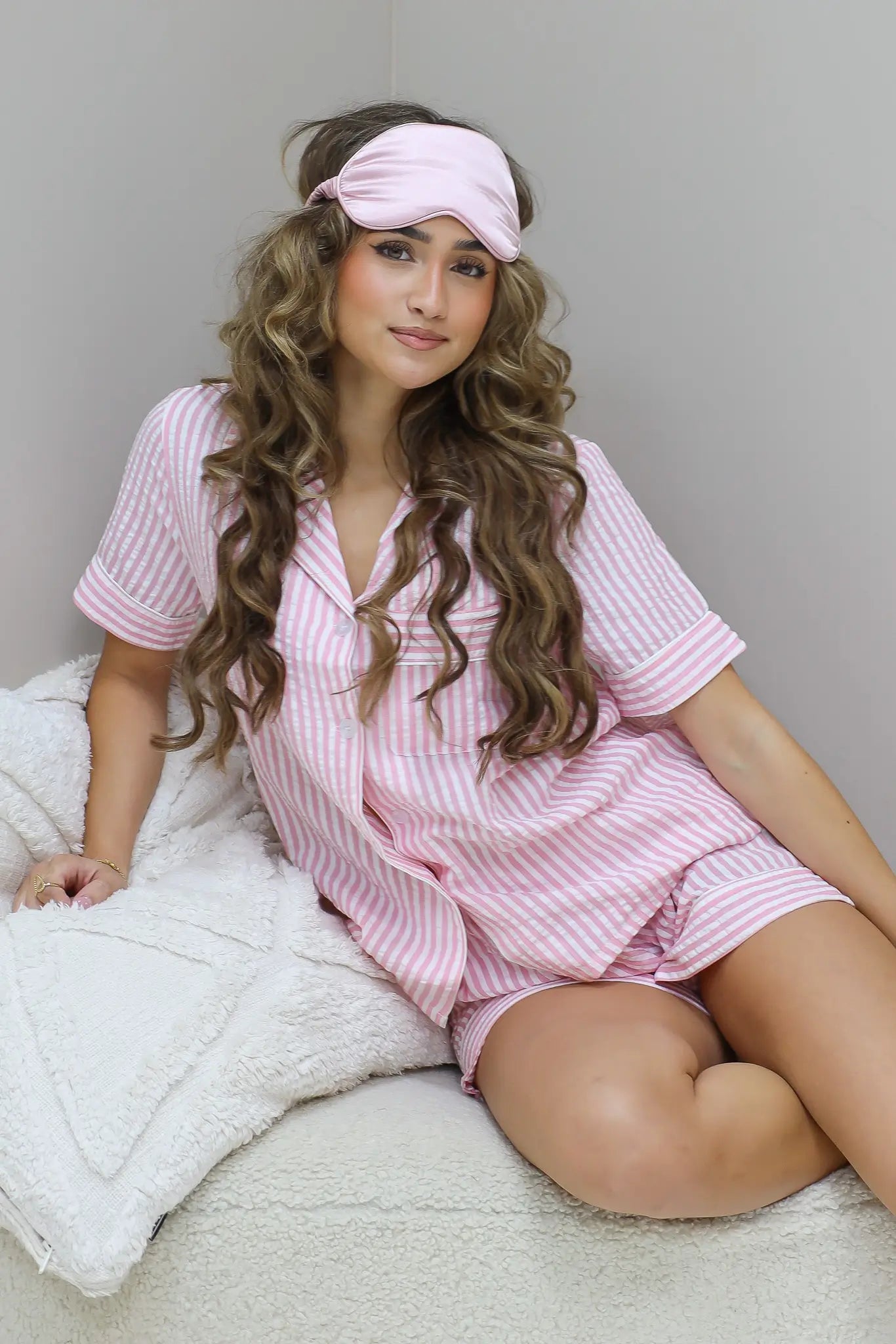Model zit op bed met roze pyjamaset en slaapmasker op hoofd