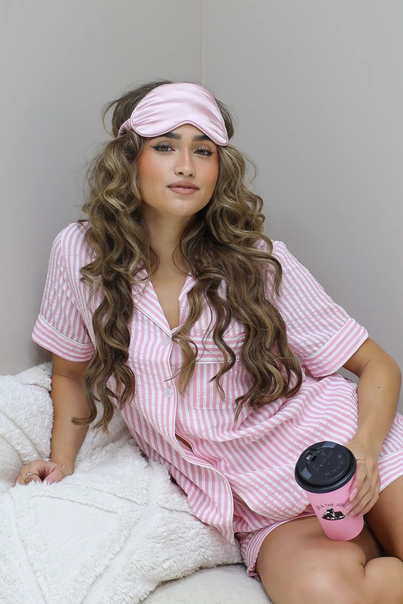 Model zit op bed met handen op schoot, glimlachend