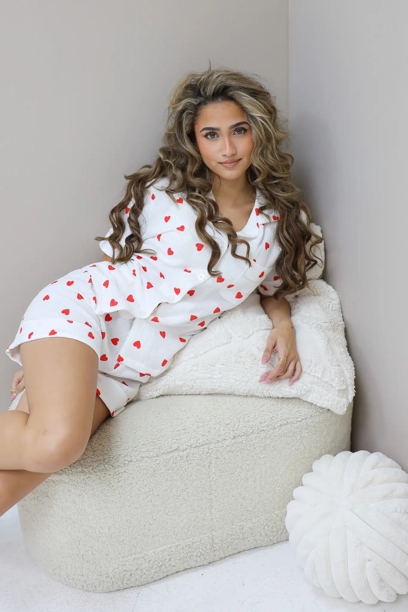 Model zit zijwaarts met hand op knie in witte pyjamaset met hartjes