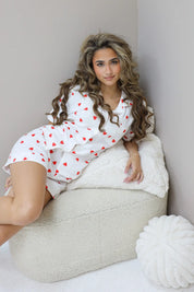 Model zit zijwaarts met hand op knie in witte pyjamaset met hartjes