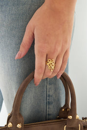 Hand met gouden bloemen ring bij spijkerbroek en bruine tas