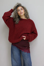 model met bordeaux trui over rode top met kant en blauwe jeans