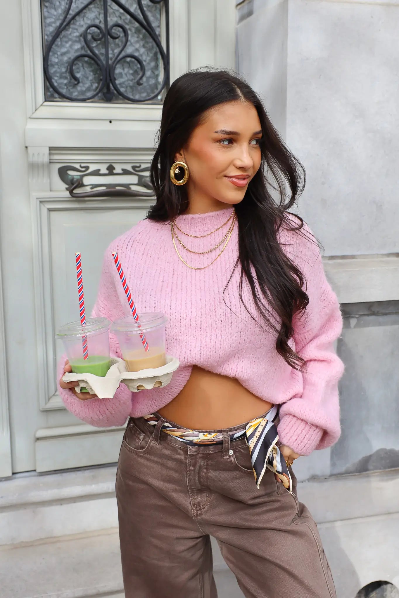 Model poseert buiten in roze fluffy trui met bruine broek en bekers