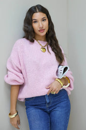 Model kijkt recht in camera in roze fluffy trui met blauwe jeans en witte tas