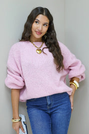 Model leunt tegen muur in roze fluffy trui met blauwe jeans