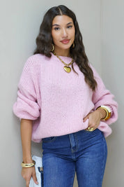 Model poseert ontspannen in roze fluffy trui met blauwe jeans en gouden ketting