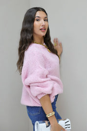 Model draait licht opzij in roze fluffy trui met blauwe jeans en witte tas in hand