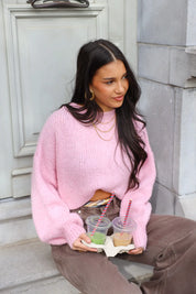 Model zit op trap in roze fluffy trui en bruine broek met beker op schoot