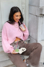 Model zit op trap met roze fluffy trui, bruine broek en kijkt opzij