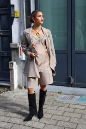 model draagt beige satijnen top met kanten rand en blazer met zwarte laarzen buiten